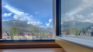 Blick durch ein Fenster auf eine Berglandschaft mit schneebedeckten Gipfeln, Häusern und Bäumen.