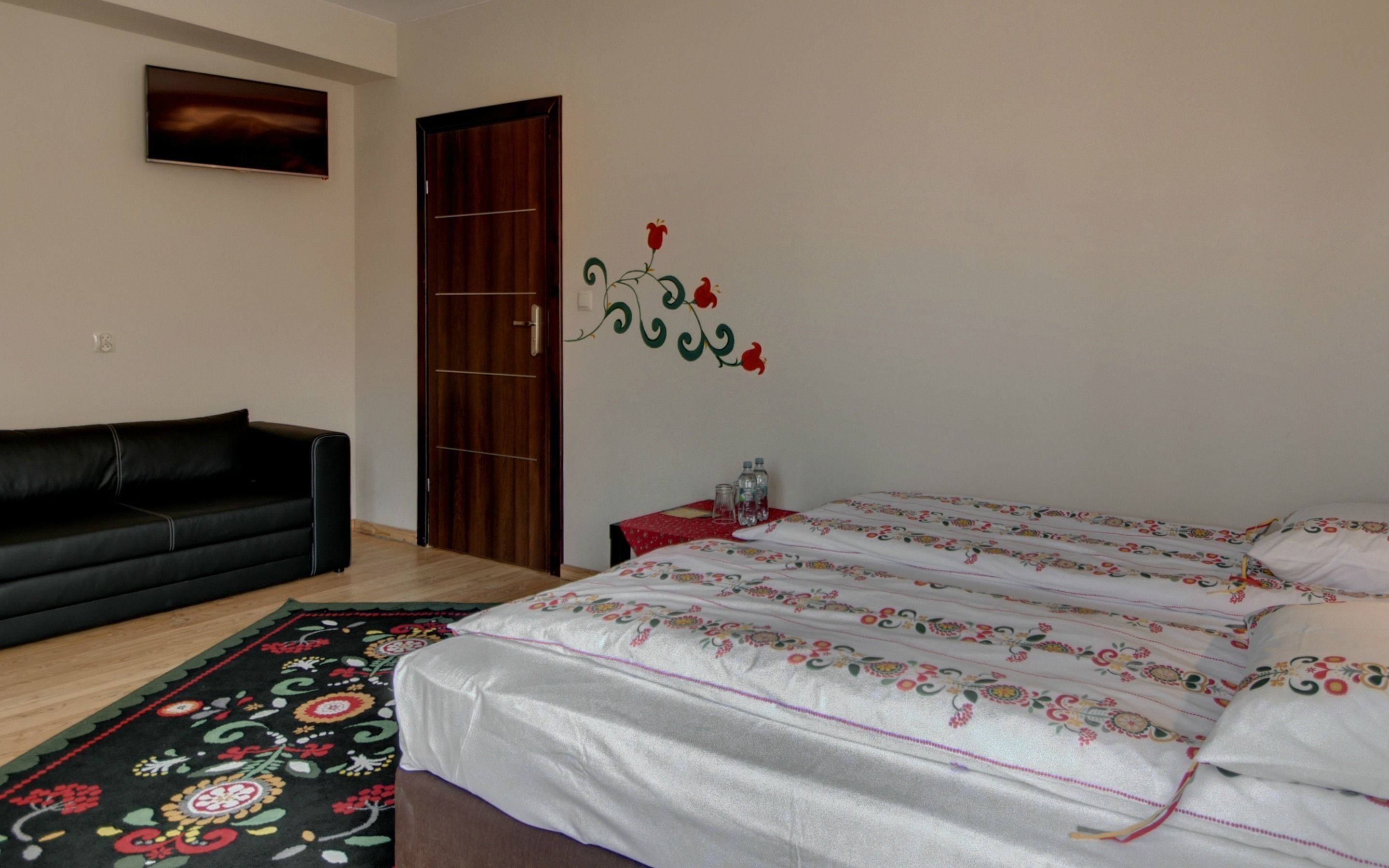 A bedroom with a bed, a black sofa, a wooden wardrobe, and a floral rug.