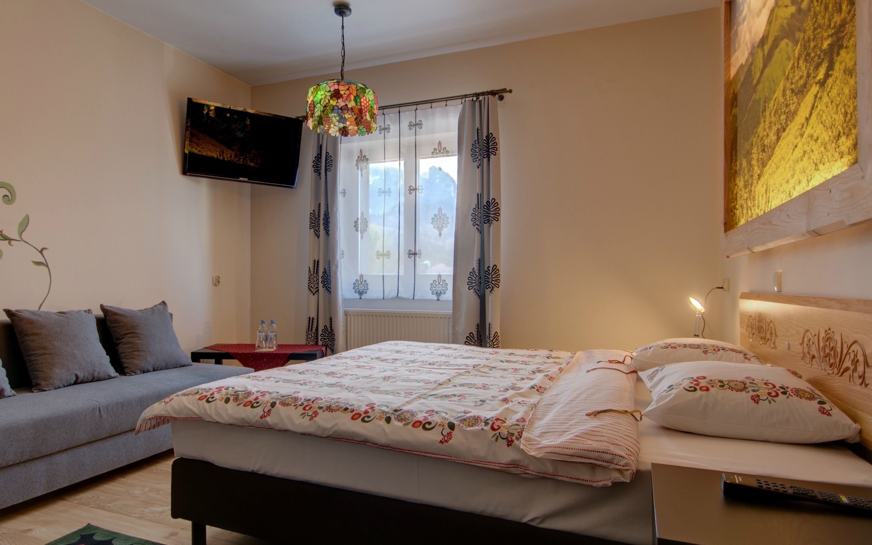 A bedroom with a bed, a sofa, a TV, and a window with curtains.