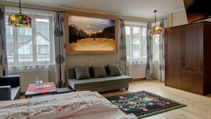 Ein Hotelzimmer mit einer Couch, einem Bett mit floralem Überwurf, einem Holzkasten, einem Fernseher und einem Gemälde einer Berglandschaft.