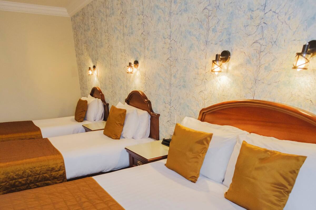 A hotel room with three beds, each with a wooden headboard, white bedding, and brown throw blankets.