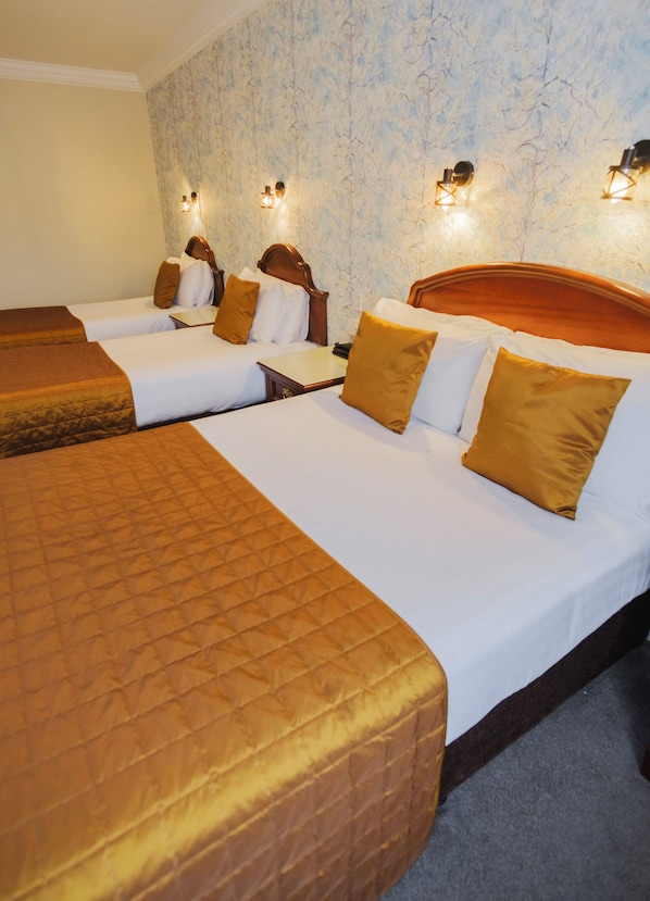 Habitación de hotel con tres camas, cada una con cabecero de madera, ropa de cama blanca y mantas marrones.