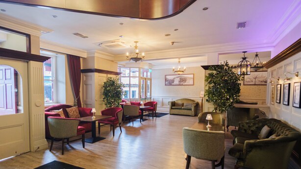 Un hall de hotel con piso de madera, asientos tapizados en rojo y verde, un árbol de Navidad y una chimenea.