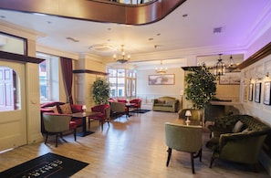 Un hall de hotel con piso de madera, asientos tapizados en rojo y verde, un árbol de Navidad y una chimenea.