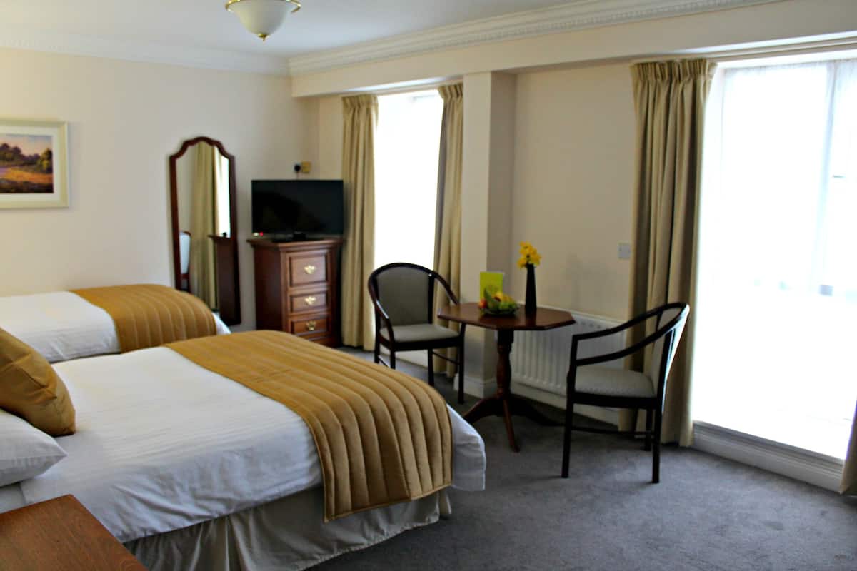 Una habitación de hotel con dos camas, televisión, escritorio con silla y ventana con cortinas.
