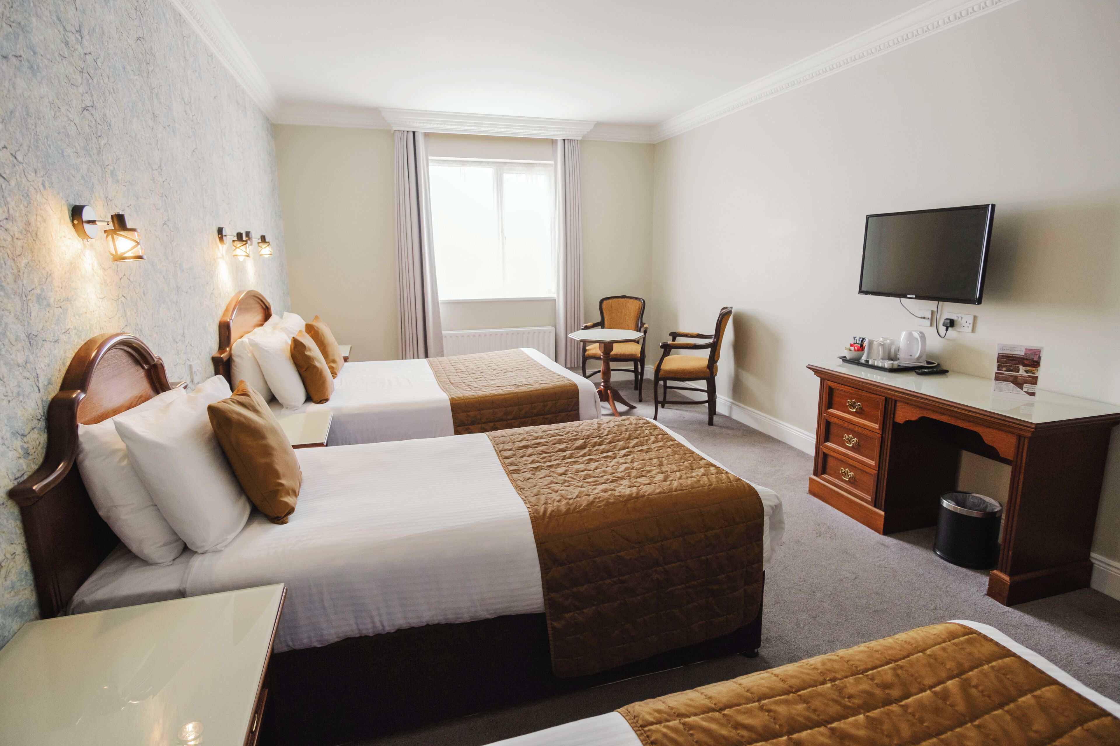 Habitación de hotel con dos camas, un escritorio, una silla, un televisor y una ventana con cortinas.