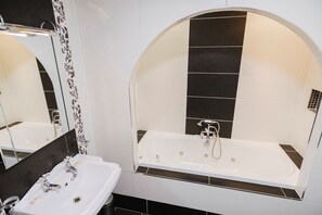 Un baño con un lavabo blanco, un espejo y una bañera con pared de azulejos blancos y negros.