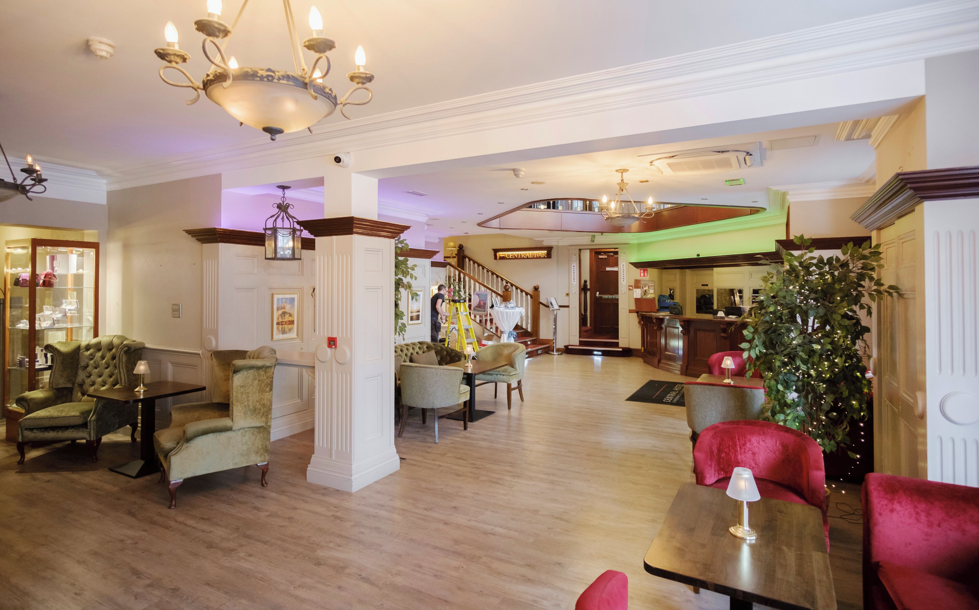 A spacious lobby with a grand chandelier, a staircase, and a reception desk.