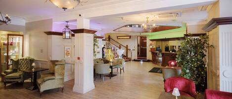 A spacious lobby with a grand chandelier, a staircase, and a reception desk.
