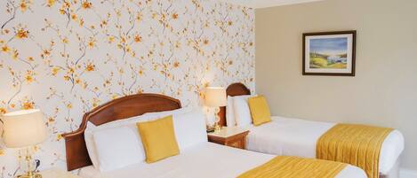 A hotel room with two beds, a nightstand, a lamp, a floral wallpaper, and a framed picture on the wall.