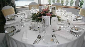 Una mesa redonda dispuesta para un evento formal, con mantel blanco, cubertería y cristalería.