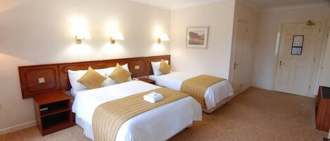 A hotel room with two beds, a wooden headboard, bedside tables, and wall-mounted lamps.