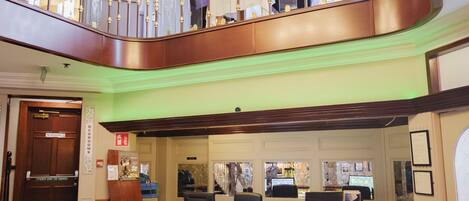 A hotel lobby with a grand chandelier, a reception desk, and a wooden staircase.