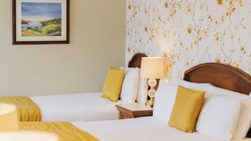 Ein Hotelzimmer mit zwei Betten, einem Nachttisch mit Lampe, einem gerahmten Bild an der Wand und einem floralen Wandpapier.