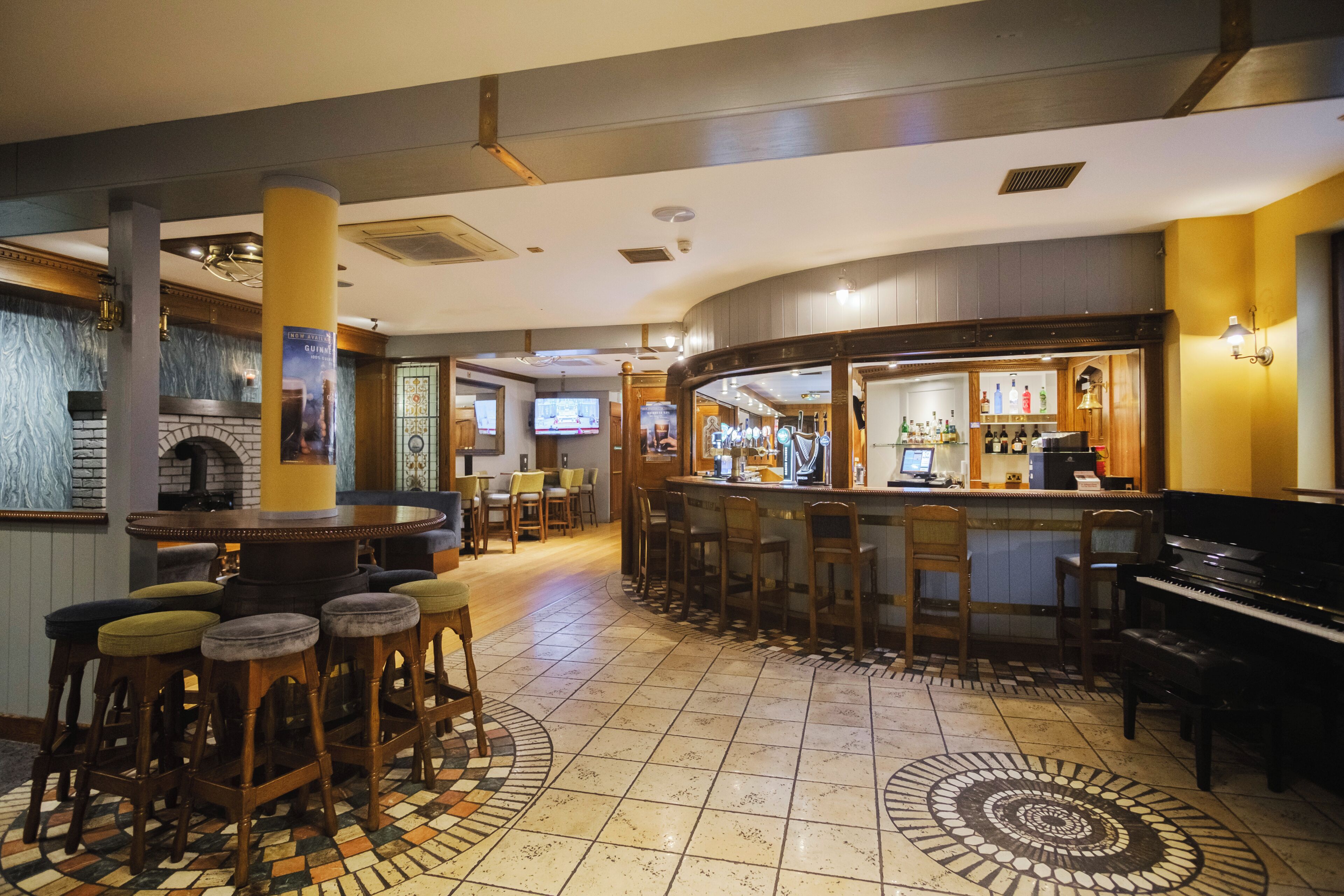 A bar area with stools, a piano, and a television screen.