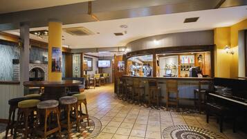A bar area with stools, a piano, and a television screen.