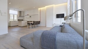 Un soggiorno moderno con un divano grigio, una TV a schermo piatto montata a parete e un'area pranzo con tavolo e sedie.