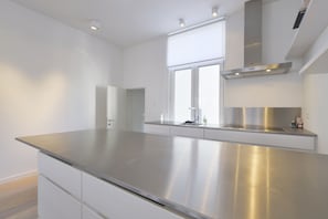 A modern kitchen with a stainless steel countertop, white cabinetry, and a window providing natural light. - Brederode Area Apartments (Antwerp)