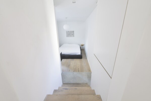 A narrow staircase leading to a bedroom with a bed, a wall-mounted light fixture, and a small artwork. - Brederode Area Apartments (Antwerp)