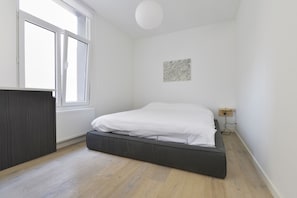 A bedroom with a bed, a window, a radiator, and a small wall-mounted artwork. - Brederode Area Apartments (Antwerp)