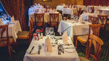 Un restaurante con varias mesas dispuestas para comer, cada una con manteles blancos, sillas de madera y cubertería ordenada.