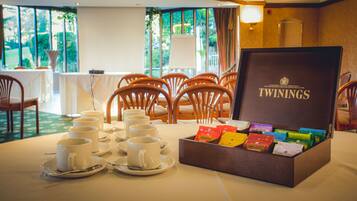 A dining area with a table set for tea service, a box labeled "TWININGS," and a view of greenery outside.