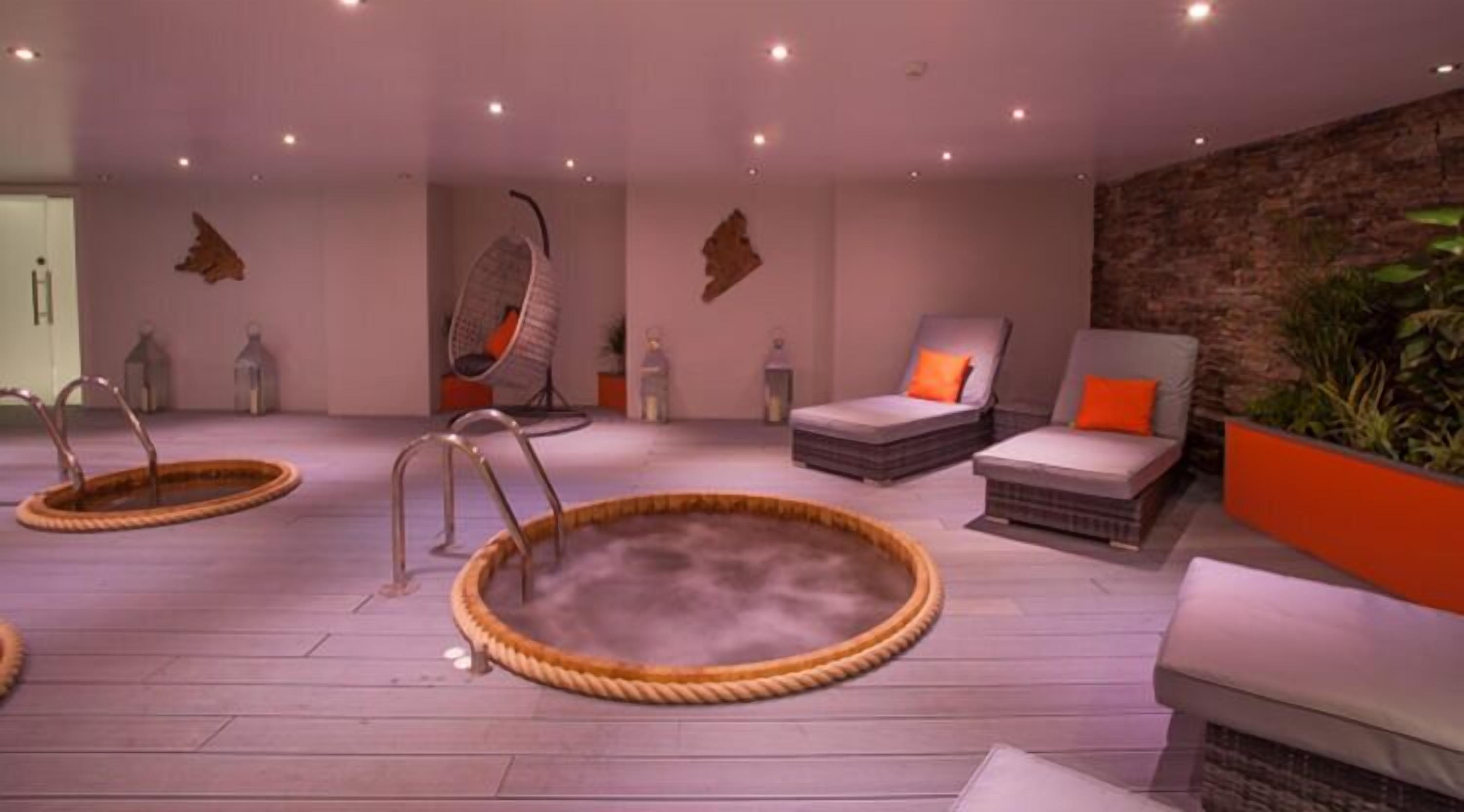 A spa area with two hot tubs, a massage chair, and a seating area with a brick wall.