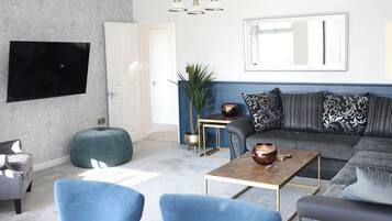Una sala de estar moderna con un sofá, dos sillones, una mesa de centro, un televisor y una planta.