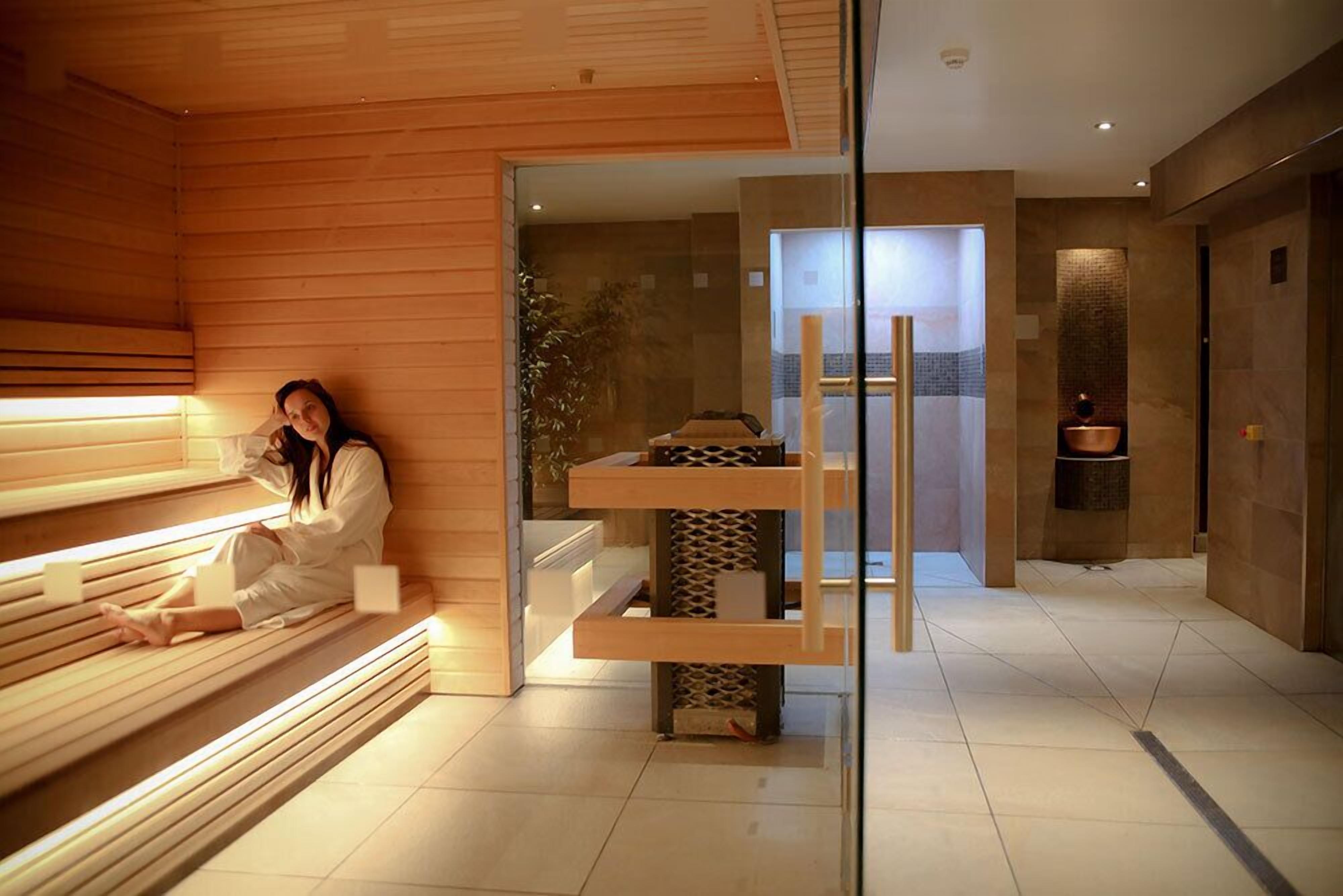 A modern interior with a wooden bench, a glass partition, and a reception area with a reception desk and a plant.
