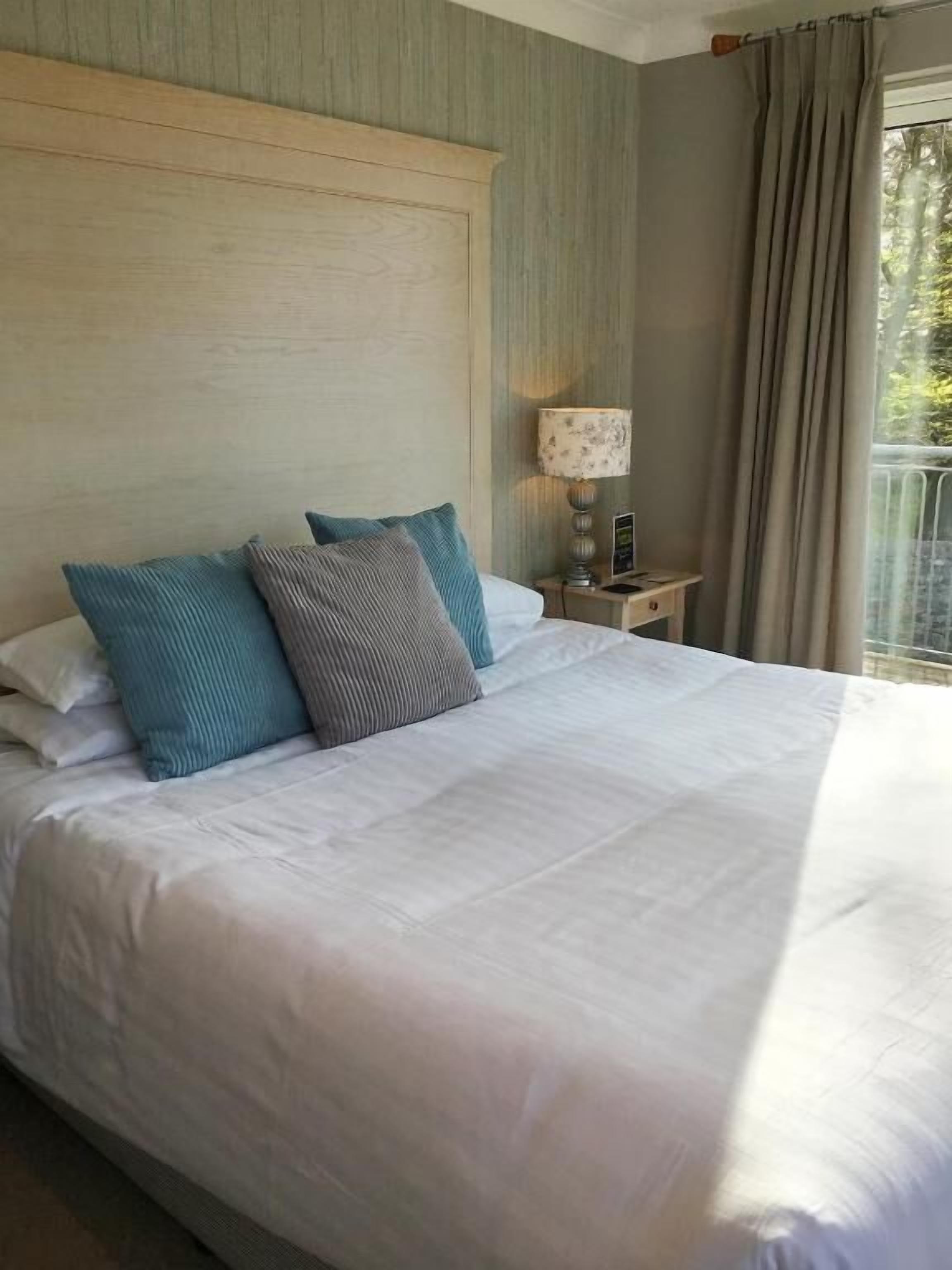 Un grand lit avec du linge de lit blanc, une tête de lit en bois et deux tables de chevet avec des lampes.