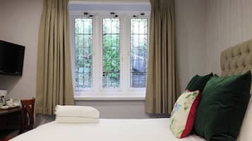 Een hotelkamer met een bed, een televisie aan de muur, een raam met gordijnen en uitzicht op groen.