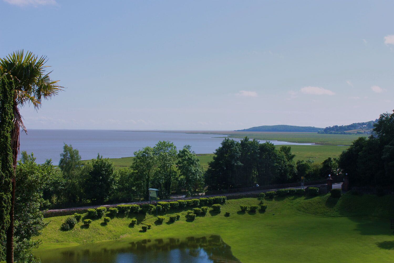 Un paysage côtier avec une étendue d’eau, des champs verdoyants et une colline à l’horizon.