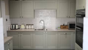 A kitchen with light grey cabinets, a white tiled backsplash, a stainless steel sink, a toaster, a kettle, and a microwave.