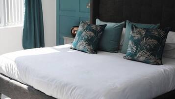 Una cama con ropa de cama blanca, almohadas turquesa y un cabecero oscuro en una habitación con paredes color turquesa y una ventana con cortinas.