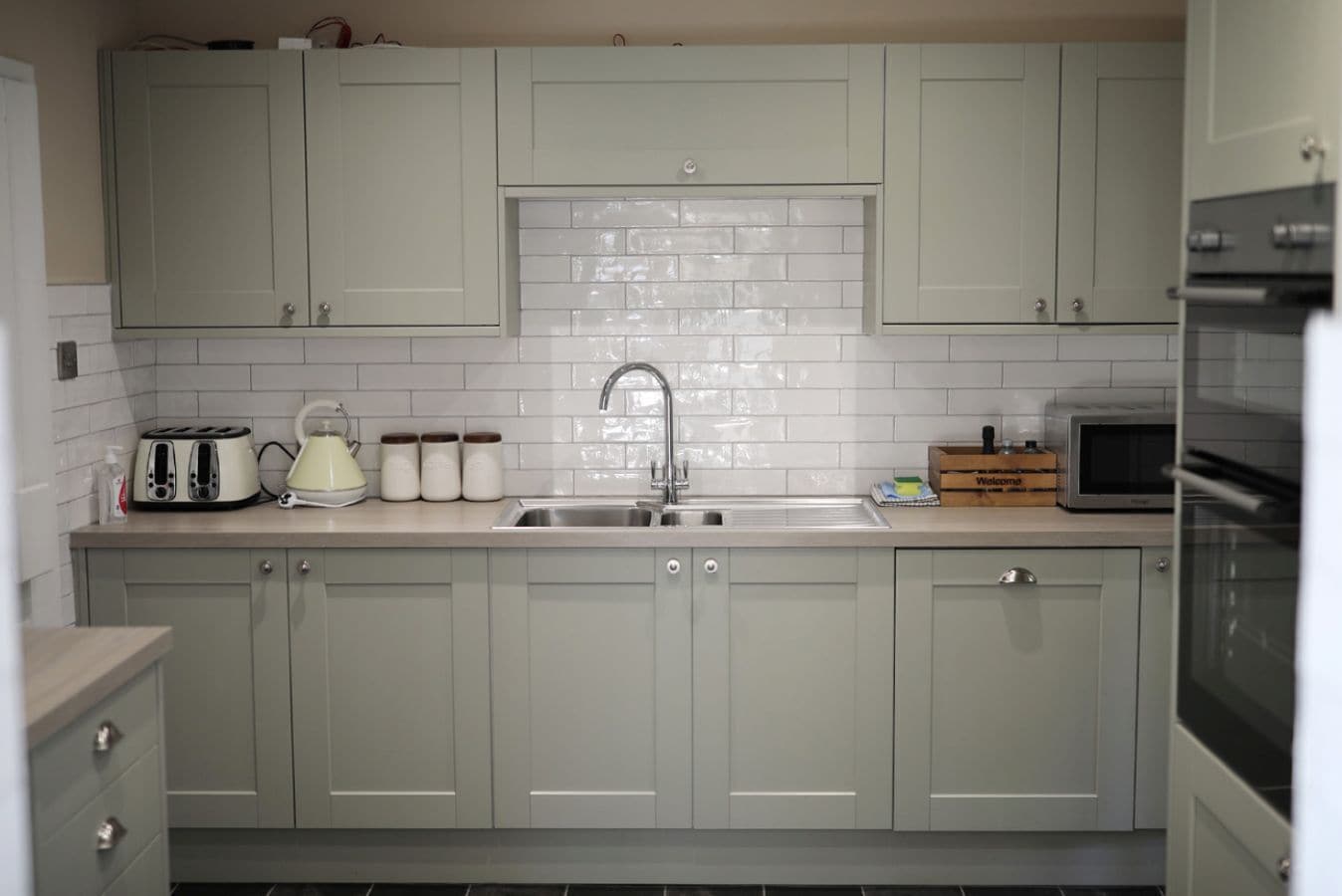 A kitchen with light grey cabinets, a stainless steel sink, a toaster, a kettle, and a microwave.