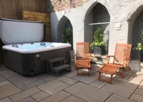 Un jacuzzi, sillas de madera y una pared de piedra con arcos.