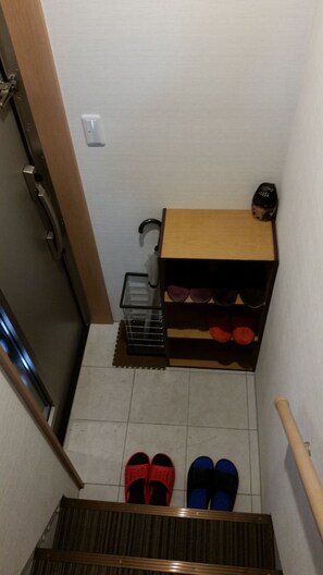 A narrow stairway leading to a room with a shoe rack, a small shelf with sunglasses, and a door with a handle. - DK House - Hostel (Fukuoka)