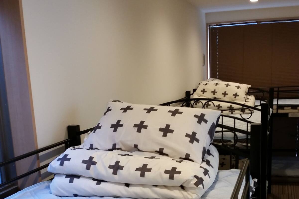 A single bed with a white quilt and black cross-patterned pillows, a wooden headboard, and a dark metal frame.