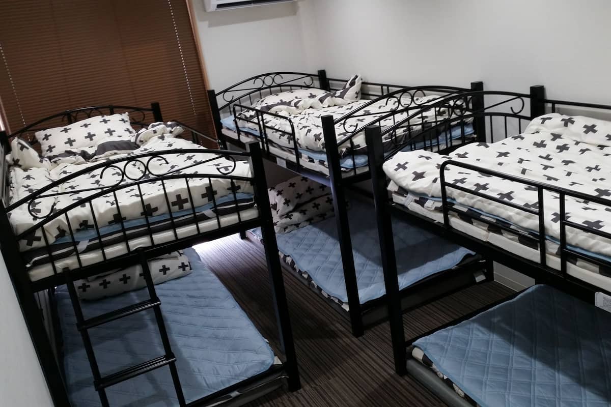 A dormitory room with four bunk beds, each with a patterned bedspread and pillows.