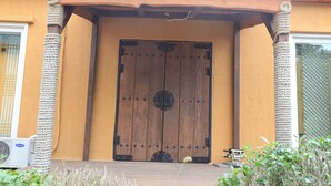 A large wooden door with a decorative metal handle, flanked by rope columns, and a small air conditioning unit to the left. - Jeju Best Hill (Jeju City)