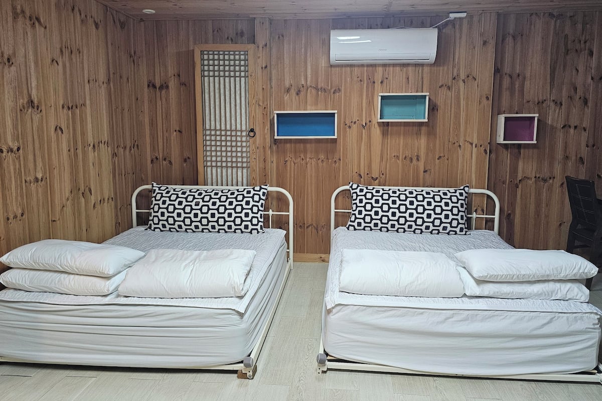 Een kamer met twee bedden, houten wanden, een airconditioning en een klein blauw plankje.