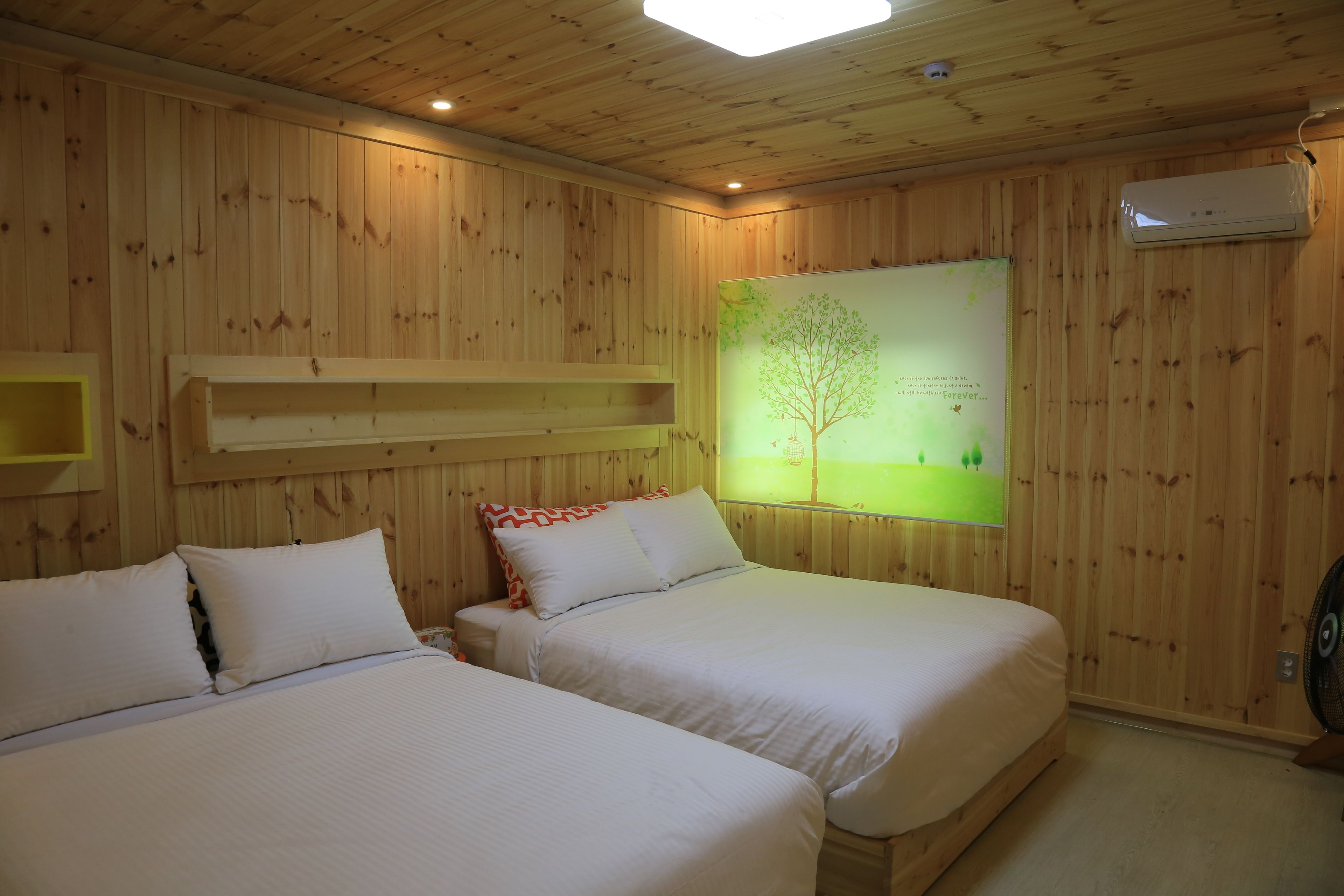A wooden-paneled room with two beds, a wall-mounted air conditioner, and a tree-themed poster.
