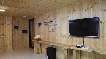 Una habitación con paneles de madera, un televisor de pantalla plana montado en la pared, un escritorio de madera con una computadora, y un estante pequeño con un reloj y una caja de pañuelos.