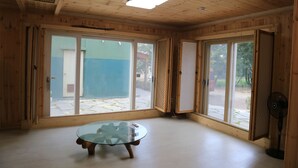 A room with wooden walls, large sliding glass doors, a glass table, and a ceiling fan. - Jeju Best Hill (Jeju City)