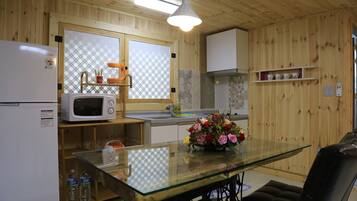 Eine Küche mit Holzwandverkleidung, einem Glastisch, einer Mikrowelle, einem Kühlschrank und einer Spüle.