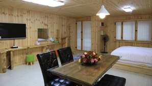 A wooden room with a bed, a dining table with chairs, a TV, and a fan. - Jeju Best Hill (Jeju City)