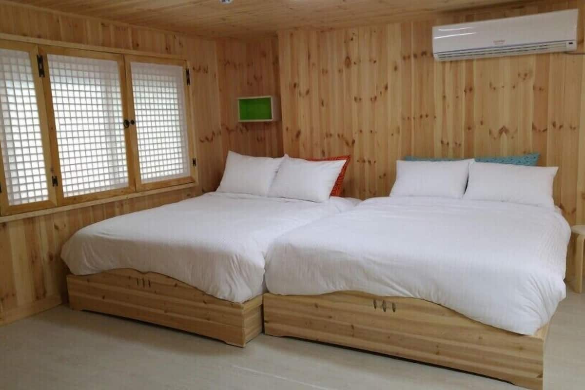Een houten kamer met twee bedden, een klein krukje en een airconditioning.