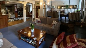A spacious living room with a large sofa, a coffee table, and a fireplace. There is a bookshelf and a dining area visible in the background. - Flambards Hotel (Cardigan)