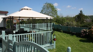 A covered outdoor seating area with a white umbrella, a light blue fence, and a well-maintained lawn. - Flambards Hotel (Cardigan)