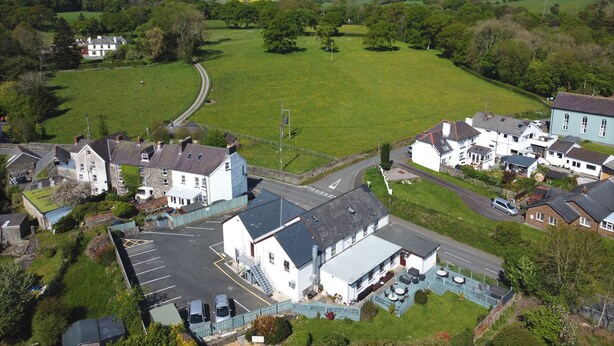 A rural village with a central white building with a blue roof, surrounded by houses and green fields. - Flambards Hotel (Cardigan)